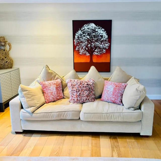 Cream lounge sofa with pink cushions beneath a tree painting